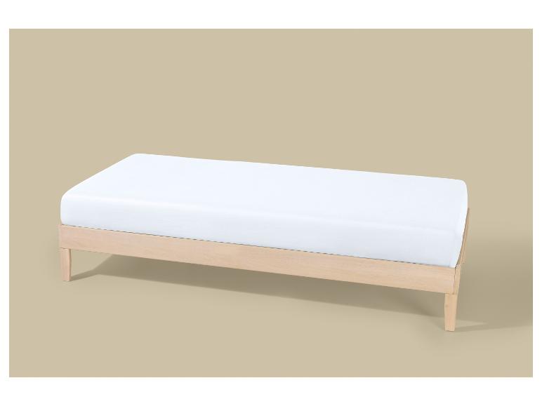 Een licht houten bedframe met een wit matras op een beige achtergrond.