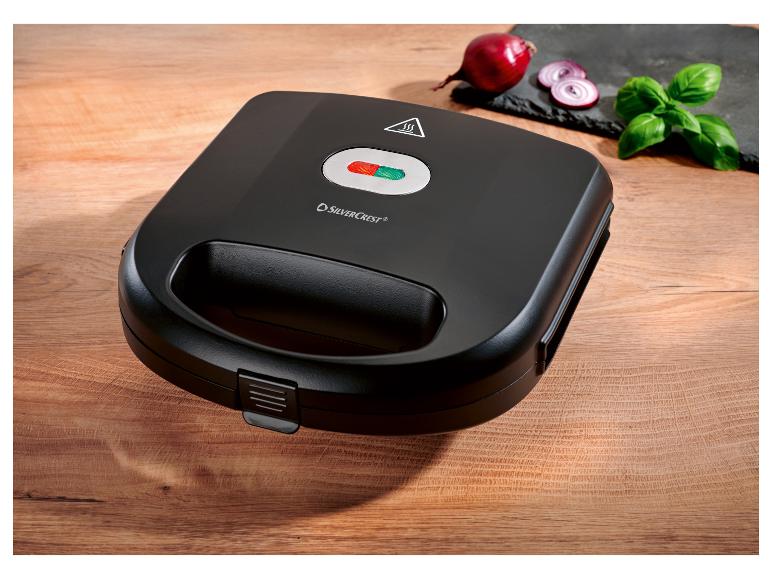 Zwarte SilverCrest tosti-ijzer op een houten tafel met ui en basilicum.