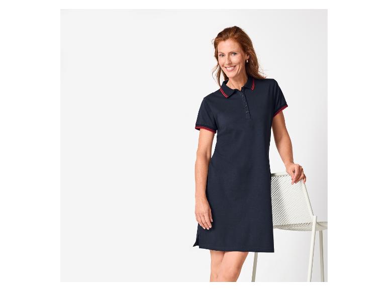 Vrouw in een marineblauwe polojurk met rode accenten, lachend, leunend op een stoel.