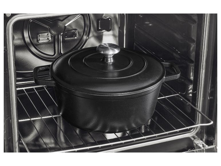 Zwarte gietijzeren pan met deksel in een oven op een metalen rooster