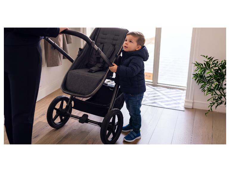 Kind in donkerblauwe jas houdt kinderwagen vast, naast een volwassene.
