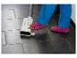 Een persoon in blauwe broek en roze sandalen gebruikt een vloerreiniger op donkere tegels.