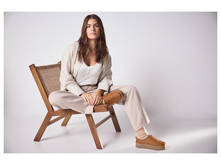 Vrouw in beige outfit en bruine platformschoenen zittend op een houten stoel.
