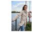 Vrouw in beige regenjas en jeans, lachend bij een meer.