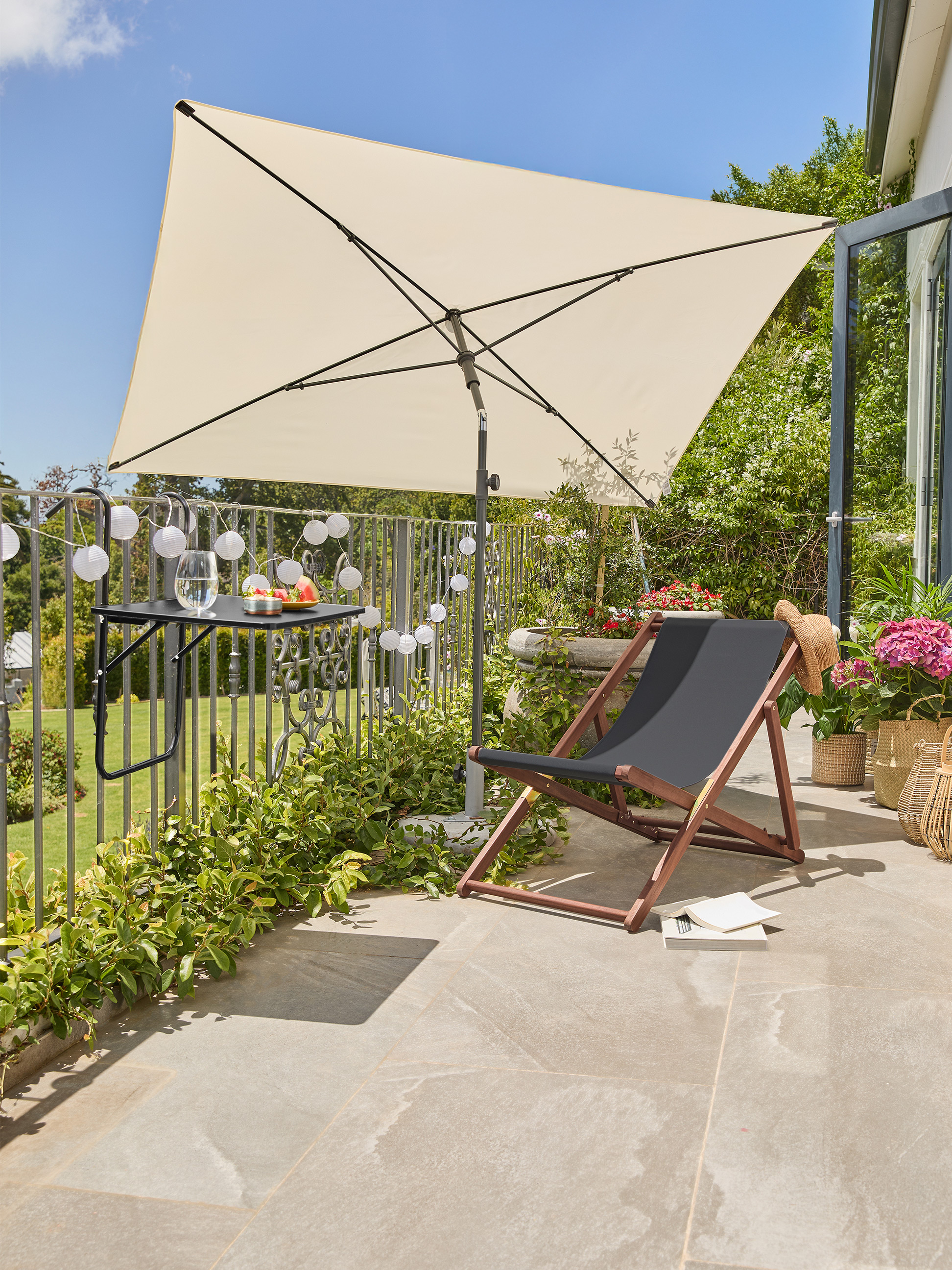 Balkon met beige parasol, zwarte ligstoel en tafel met drankjes en fruit.