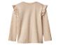 Beige kinderblouse met lange mouwen en ruches op de schouders.