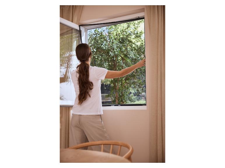 Vrouw opent raam met hor, groen buiten.