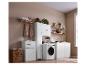 Witte wasruimte met een wasmachine, kasten, planken en een gevlochten wasmand.