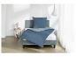 Bed met blauw dekbedovertrek en kussen, nachtkastje met lamp en witte gordijnen.