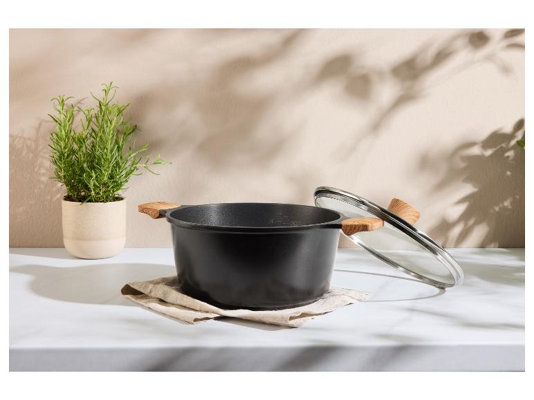 Zwarte pan met houten handvatten en glazen deksel, met een rozemarijnplant ernaast