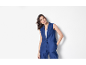 Vrouw in marineblauwe gilet en broek, poserend met een hand in haar zak.