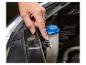 Een hand drukt een zwarte plastic clip in op het ruitensproeiervloeistofreservoir van een auto.