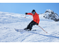 Man skiet van een besneeuwde helling, draagt een rode ski-jas, zwarte skibroek en een helm.