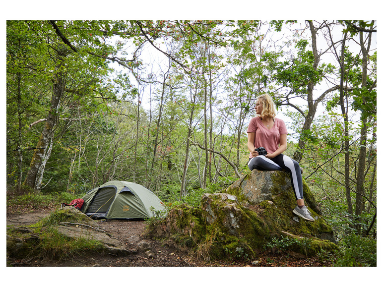 Een vrouw met een camera zit op een rots naast een Grand Canyon-tent in het bos.