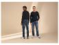 Twee mannen in shirts met lange mouwen en jeans, de een kijkt om, de ander lacht.