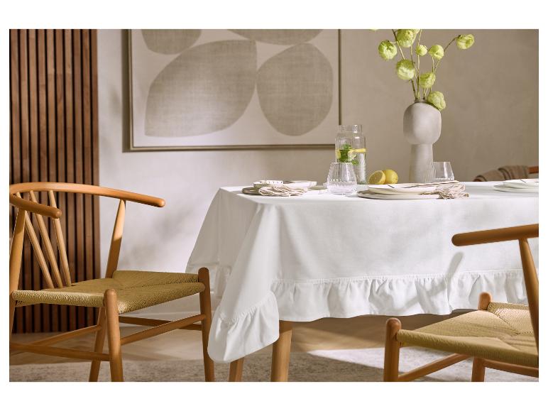 Eettafel met wit tafelkleed, servies, vaas met bloemen en houten stoelen.