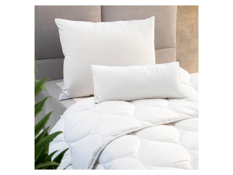 Witte kussens en dekbed op een bed met een grijs hoofdbord.