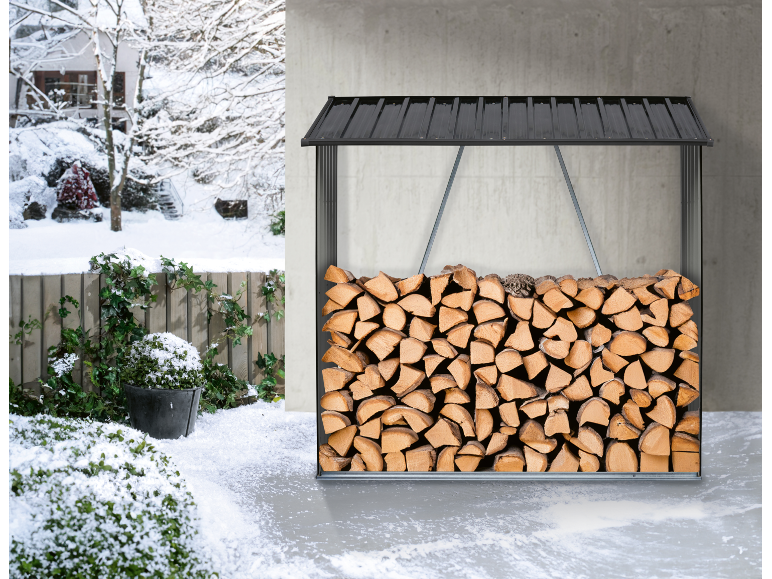 Gestapeld brandhout in een zwart houtrek, met een besneeuwd winterlandschap op de achtergrond.