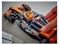 Een hand plaatst een minifiguur in een zwart-oranje LEGO McLaren raceauto.