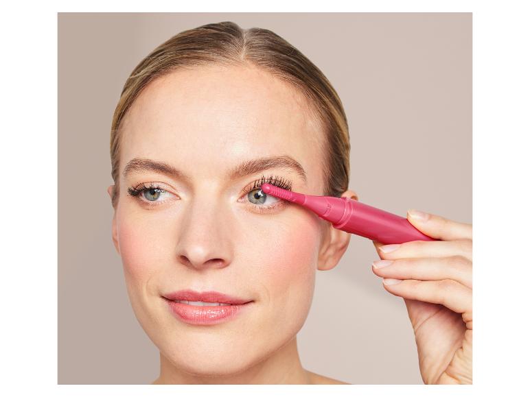 Een vrouw gebruikt een roze wimperkruller voor haar oogmake-up.