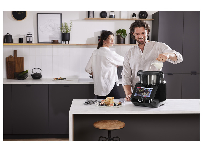 Een man giet melk in een zwarte Thermomix-keukenmachine.