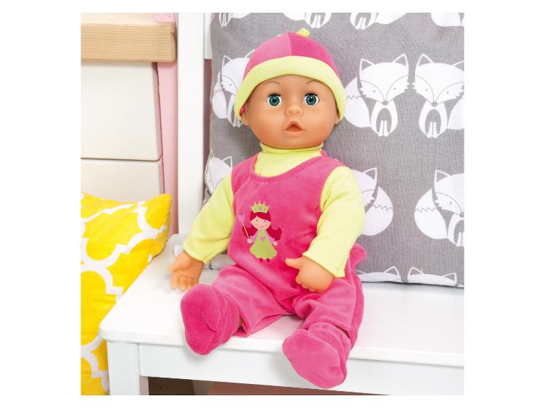 Babypop in roze en limoengroene outfit met prinsessenmotief, zittend op een wit bankje.