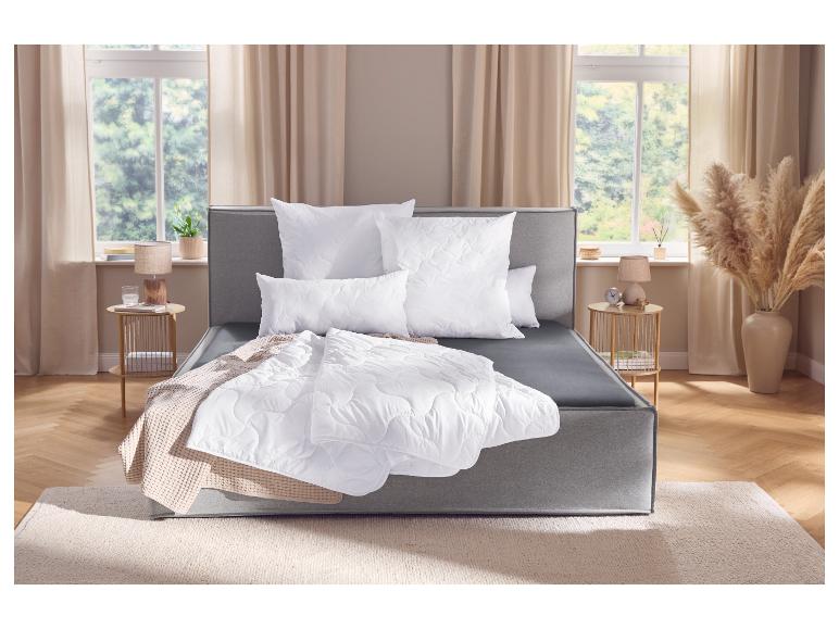 Grijs boxspringbed met wit beddengoed en sprei in een slaapkamer met raam.
