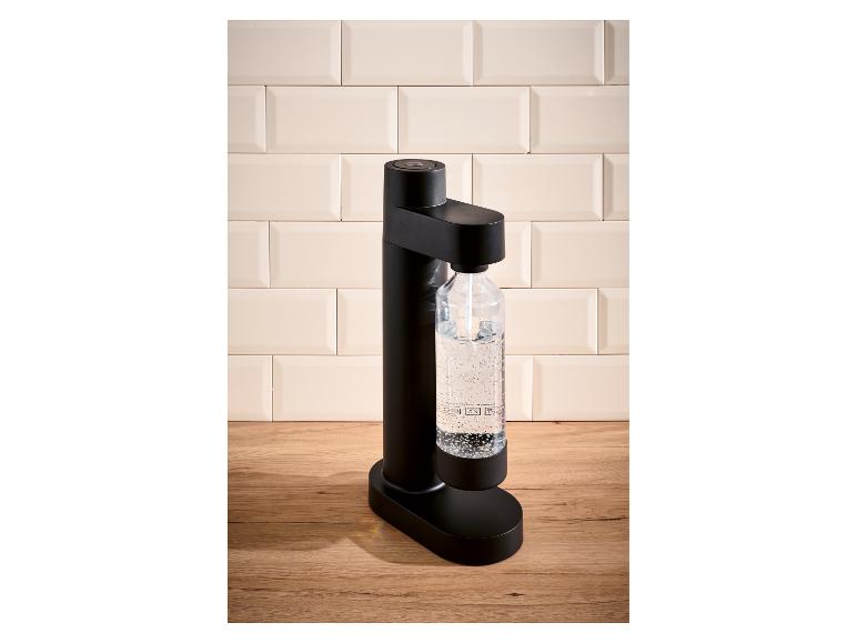 Zwart sodawaterapparaat met een fles bruiswater op een houten aanrecht