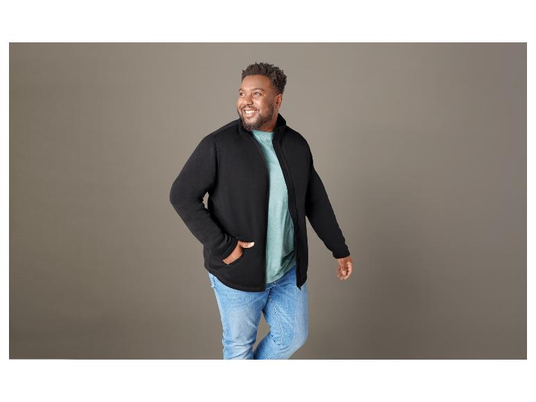 Man draagt een zwarte trui met rits en blauwe jeans.