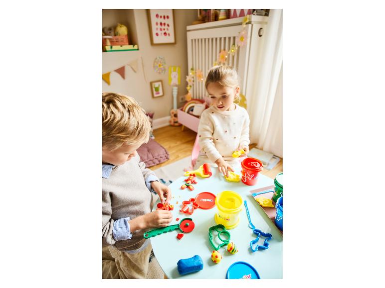 Twee kinderen spelen met Play-Doh klei en uitsteekvormpjes aan een lichtblauwe tafel.