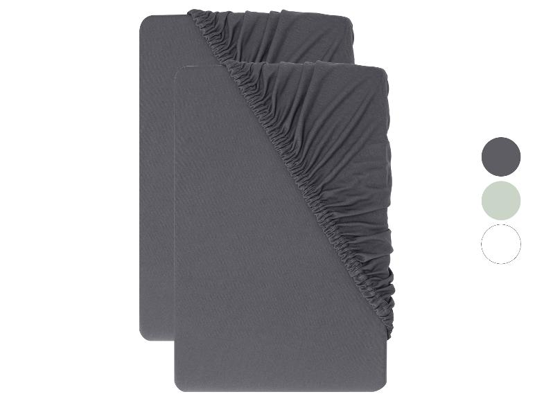 Twee grijze hoeslakens met elastiek in de hoeken, met kleurstalen in grijs, lichtgroen en wit.