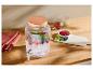Glazen drankdispenser met bessen en munt, glazen en fruit op een houten tafel.