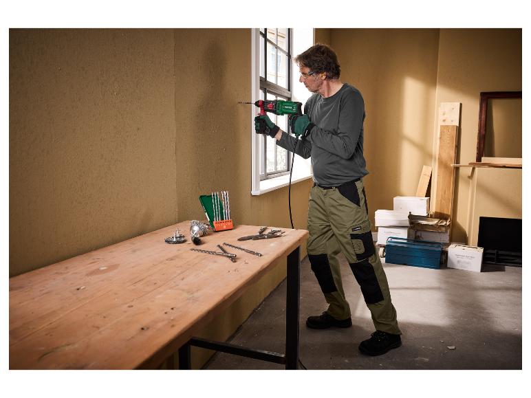 Man met handschoenen en veiligheidsbril boort een muur met een Parkside boormachine.
