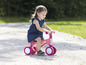 Een jong meisje rijdt op een roze loopfiets met witte wielen.