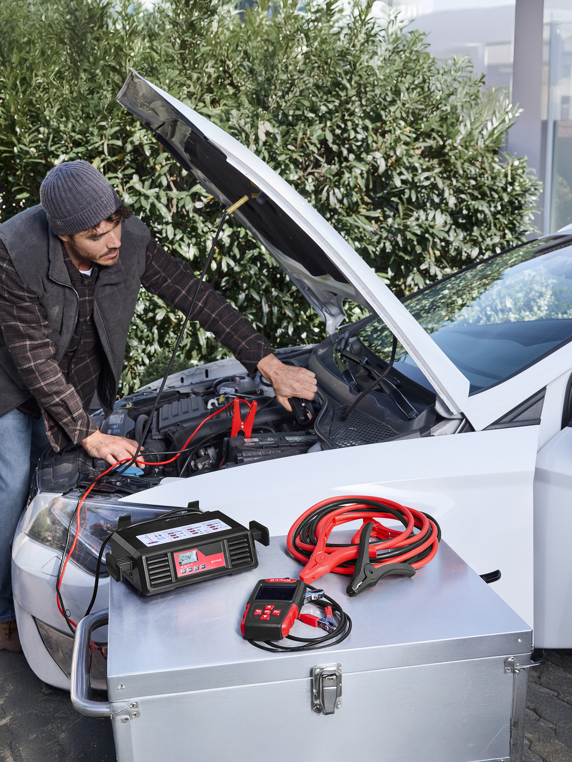 Man gebruikt ULTIMATE SPEED autolader en startkabels bij een auto.