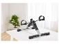 Mini hometrainer met digitaal display op een witte tafel, met een plant op de achtergrond.