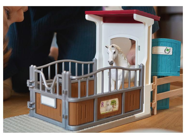 Kind speelt met een speelgoedpaardenstal met een wit paard.