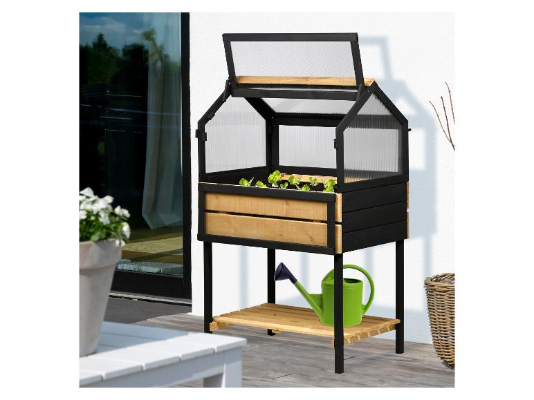 Verhoogde zwarte en natuurhouten minikas met planten en groene gieter op een terras.