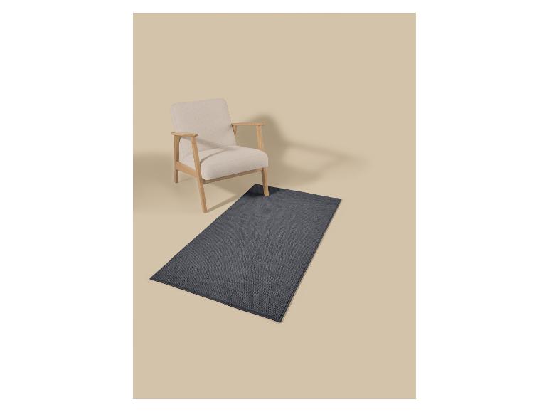 Lichte houten fauteuil met beige kussens en een donkergrijs rechthoekig vloerkleed.