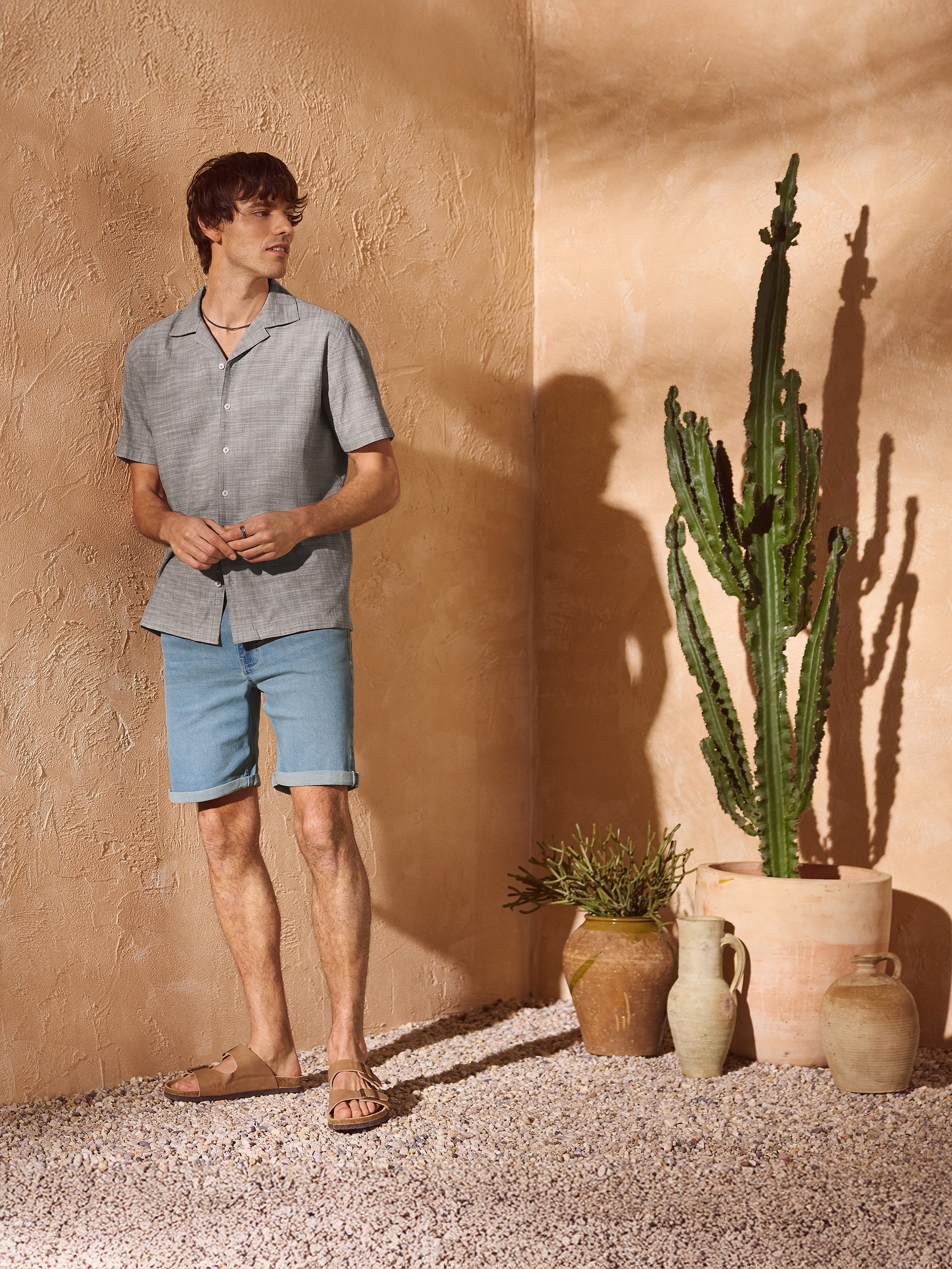 Man in grijs overhemd en spijkerbroek, sandalen, in mediterrane sfeer.