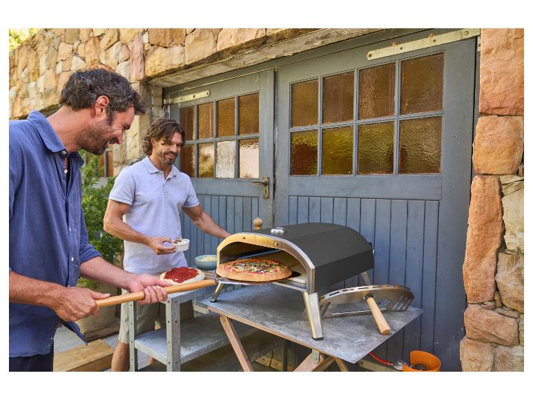 Twee mannen bereiden pizza's buiten met een buitenpizzaoven.