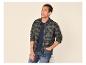 Man in een groen geruit overhemd en blauwe jeans, lachend en opzij kijkend.