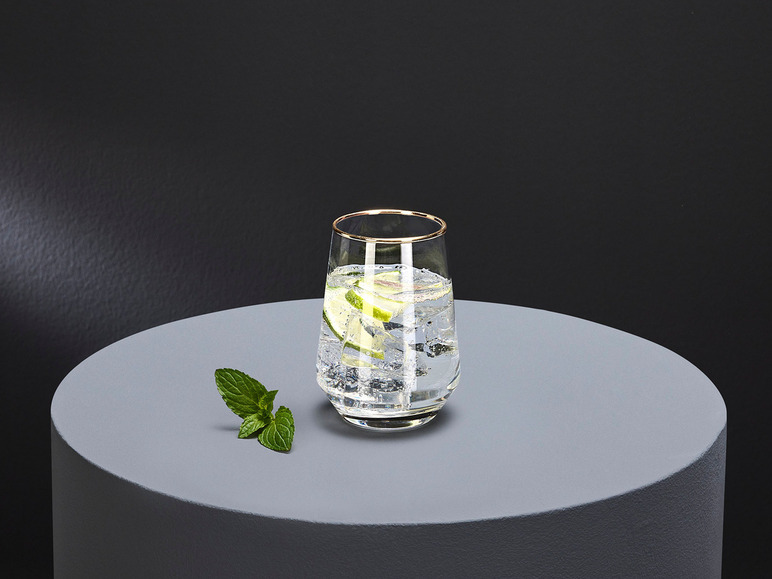 Een glas met gouden rand, gevuld met ijs en limoen, op een grijze ondergrond.