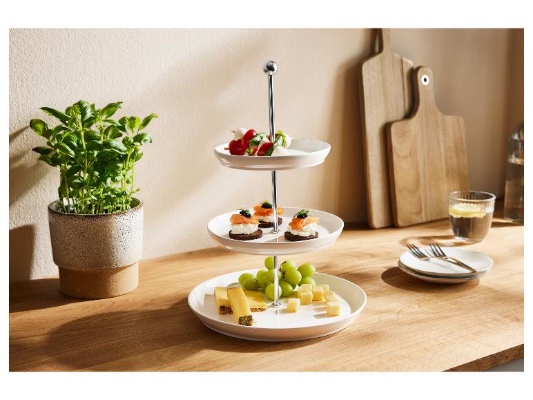 Een drielaags etagère gevuld met hapjes, kaas en druiven, op een houten tafel.