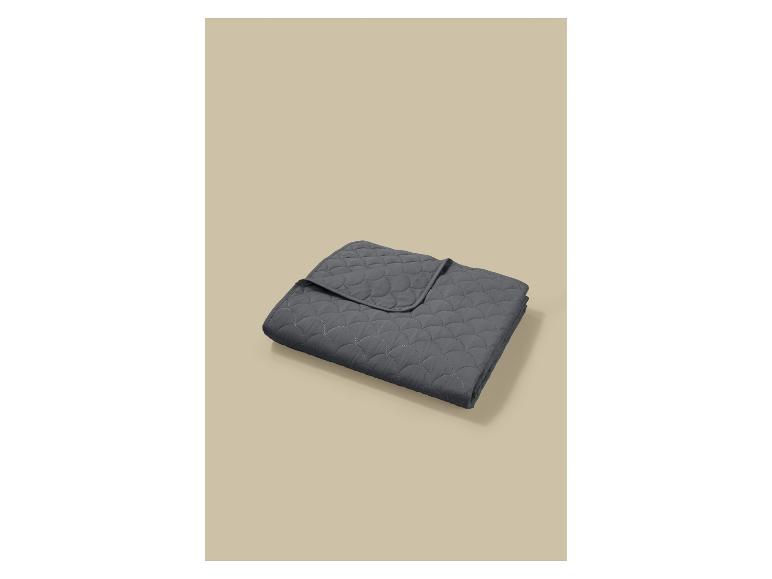 Donkergrijze gewatteerde deken met een schelpenpatroon, opgevouwen op een beige achtergrond.