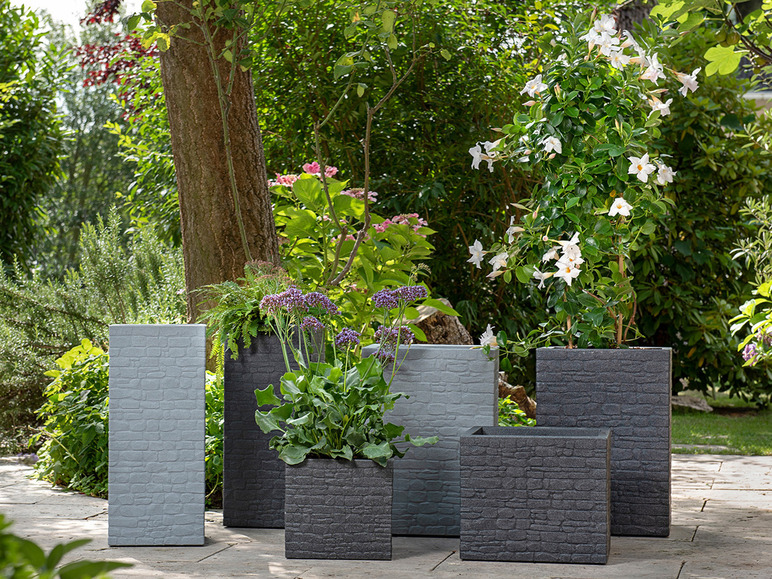 Stenen plantenbakken in verschillende maten en kleuren in een tuinomgeving.