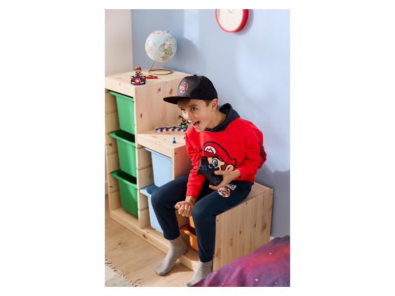 Jongen in rode hoodie en donkerblauwe broek speelt videogames op een houten rek.