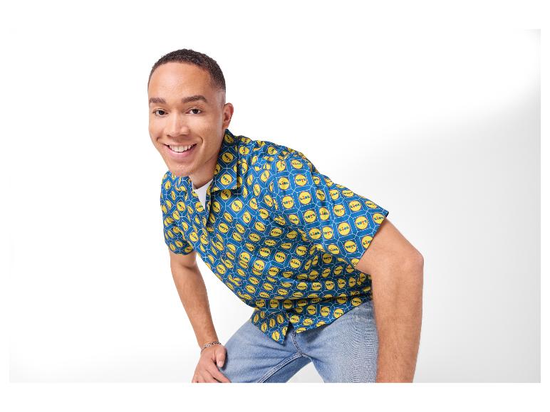 Man in een blauw overhemd met gele logo's, lachend naar de camera.