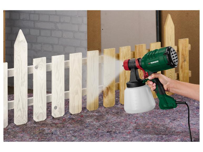 Persoon spuit een houten hek wit met een Parkside verfspuit.