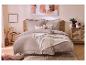 Beige beddengoed met ruches en sprei op een bed met rotan hoofdeinde in een slaapkamer.